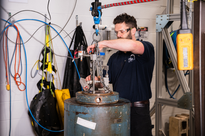 Technician performing pressure testing on industrial equipment using a suspended test rig inside a laboratory environment.